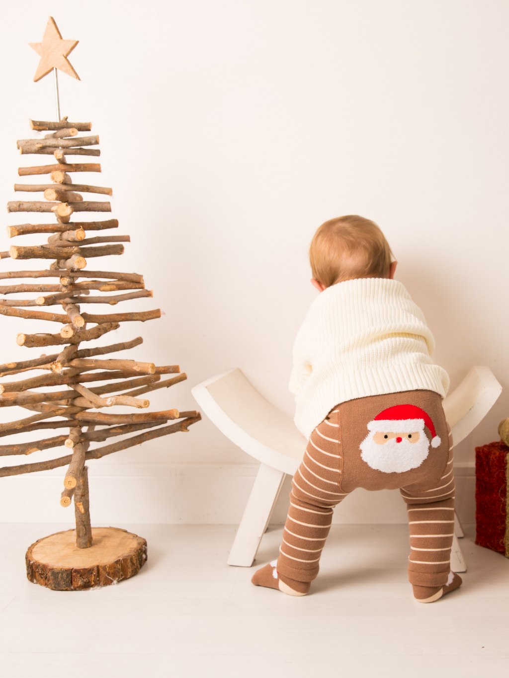 Baby wearing the Santa Ho Ho Ho Leggings beside a wooden Christmas tree